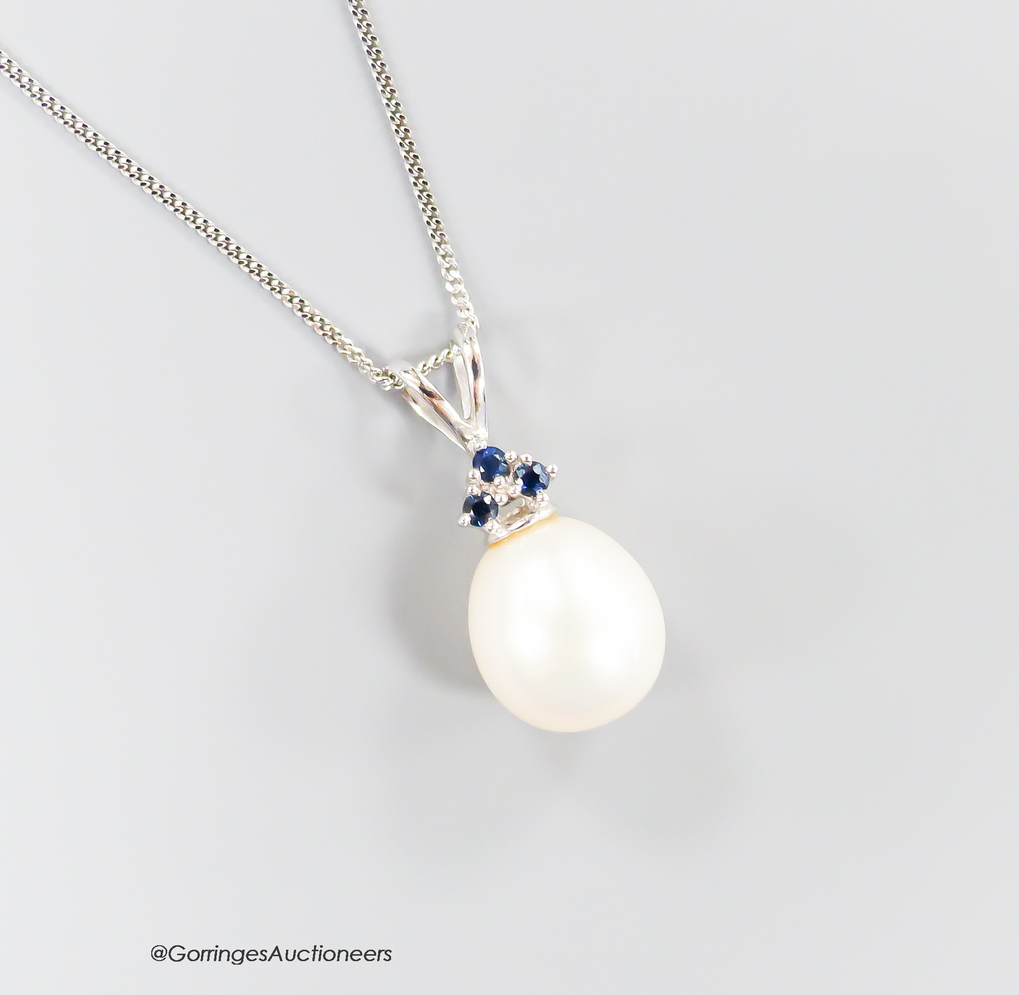 A modern Moire 375 white metal, single stone cultured pearl and three stone sapphire set pendant, 20mm, on a 375 chain, 43cm.